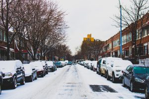 district 7: snow in the street with cars lining it and snow on top