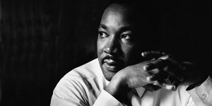 black and white image of martin luther king looking in the distance with his hands clasped
