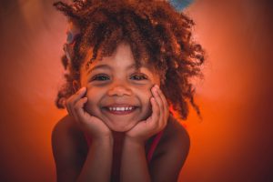 Lexus: little girl smiling with a little afro and a burnt orange background