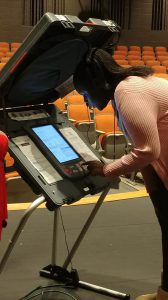 Citizens Youth Academy: a young girl in a light pink cardigan working a voting machine