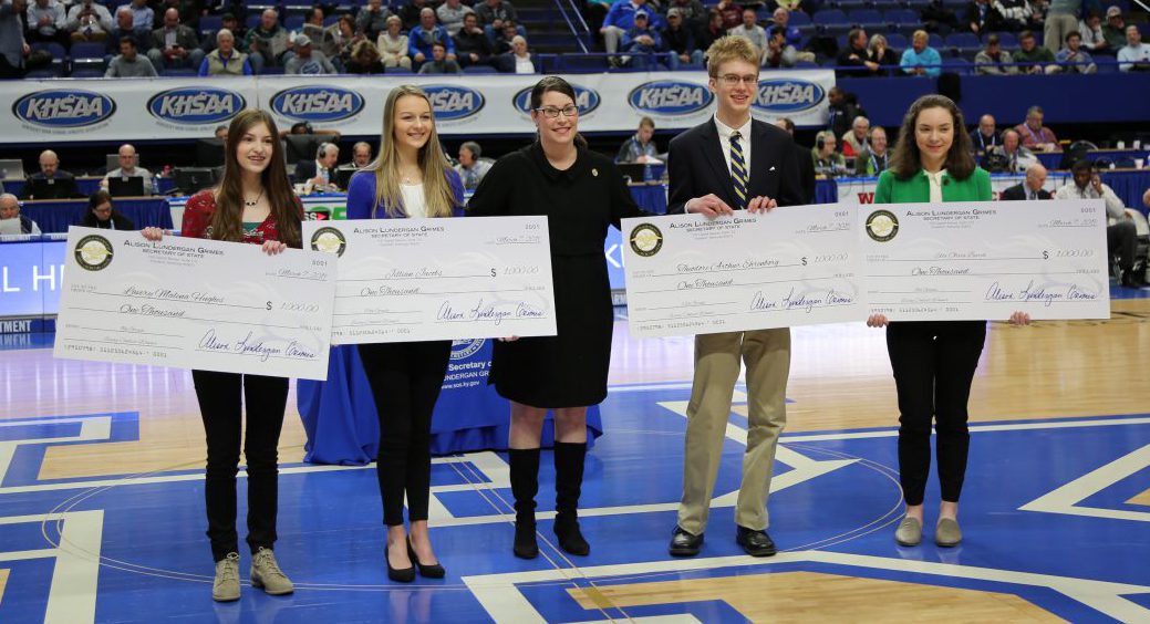 Essay Contest: four students holding checks and a woman dressed in black between them