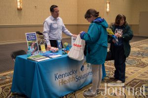 Senior: a man at a table that says kentucky health solutions on the table cloth talking with a female