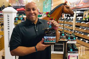 Total Wine: a man in a black polo holding a bottle of bourbon with a fake horse behind him