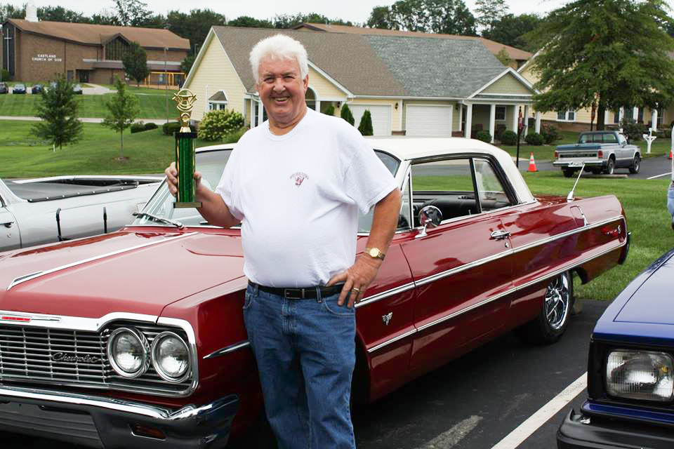 Senior: man with a trophy in front of a classic car