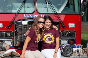 Family: two women in maroon shirts sitting in front of a fire truck smiling at a camera